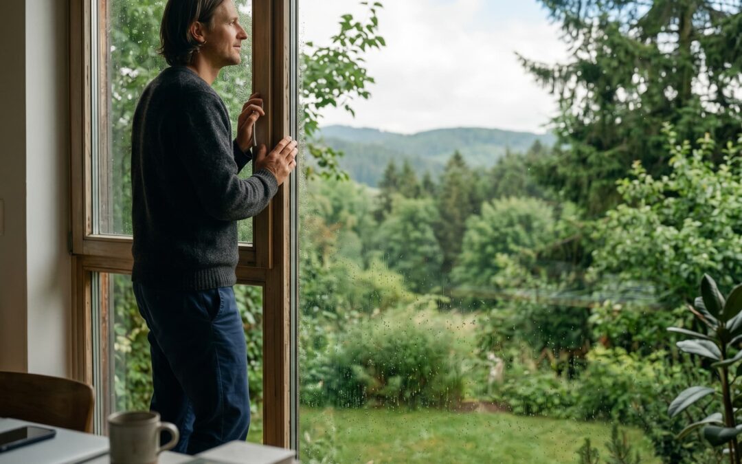 Ein Mann blickt aus einem regennassen Fenster in einen klaren, grünen Garten – Symbol für Präsenz und innere Klärung.